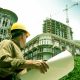 An Architect observes the large building with a plan on his hand.