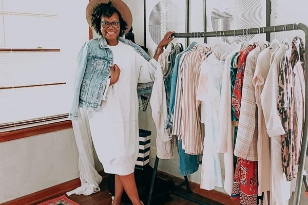 A woman is standing nearby a long hanger where clothes are hung.